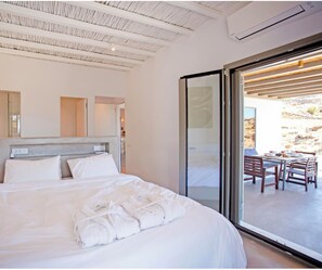 A modern bedroom with a large bed, a sliding glass door leading to an outdoor seating area. - Villa Ibti 6 bedrooms Private Pool (Ermoupoli)