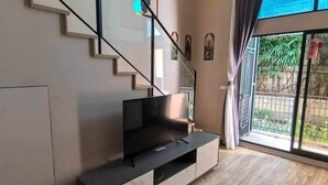 Un salon moderne avec un escalier, un téléviseur à écran plat et une grande fenêtre avec des rideaux.