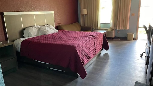 A hotel room with a bed, a nightstand, a lamp, a chair, and a window with curtains.