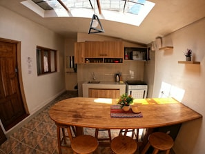 A compact kitchen with wooden cabinets, a built-in microwave, and a small oven. There is a round wooden table with stools and a potted plant on it. - EKEKOS CUSCO (Cusco)