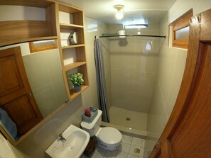 Une salle de bain équipée d’une douche, de toilettes, d’un lavabo et d’étagères en bois.