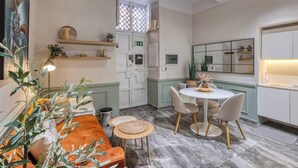 Een knus ingerichte kamer met een bank, een ronde eettafel met stoelen, een bijzettafeltje en een spiegel aan de muur.