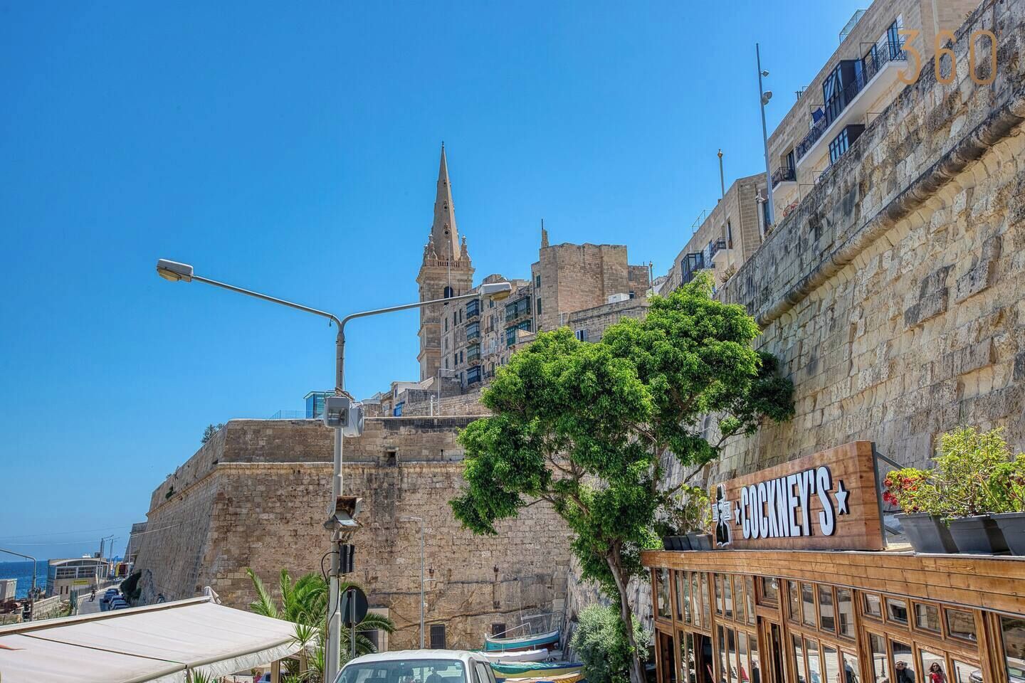 A coastal cityscape with historic stone buildings, a prominent church spire, and a restaurant named 'COKKELT'S'.