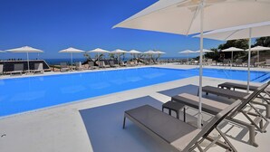 Zona de piscina con sillones de descanso y sombrillas, cielo azul despejado y vista al mar.