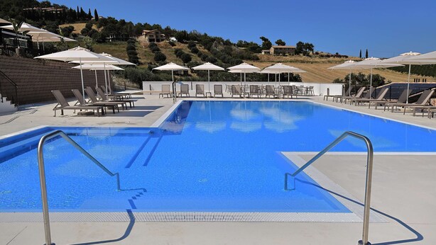 Piscina con sillones de descanso y sombrillas, rodeada por una ladera.