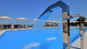 Una piscina con agua cristalina y azul, rodeada de tumbonas y sombrillas.