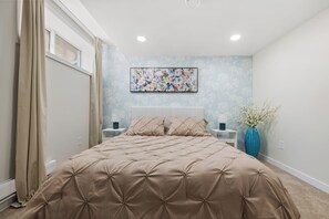 A bedroom with a large bed, a nightstand, a vase with flowers, and a wall-mounted painting.