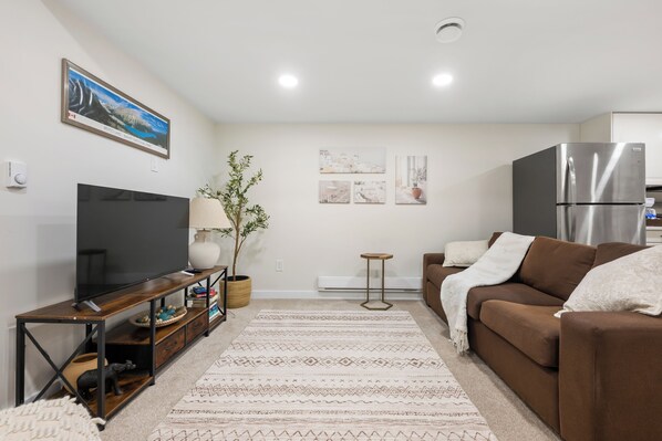 A living room with a flat-screen TV, a brown sofa, a coffee table, and a decorative plant.