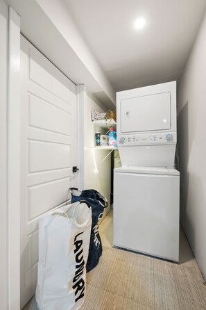Ein Waschraum mit Waschmaschine und Trockner, einer Tür und einer Tasche mit der Aufschrift 'LAUNDRY' auf dem Boden.