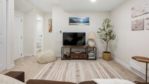 A living room with a flat-screen TV, a lamp, a potted plant, and a framed picture on the wall.