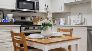 A modern kitchen with white cabinetry, a stainless steel microwave, a stove, and a dining table set with plates and a vase of flowers.