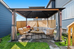 A covered patio area with a table and chairs, a barbecue grill, and a pergola overhead. - Pristine Suite Near Fish Creek Park & Horse Events (500 Mbps WiFi + Workspace) (Calgary)