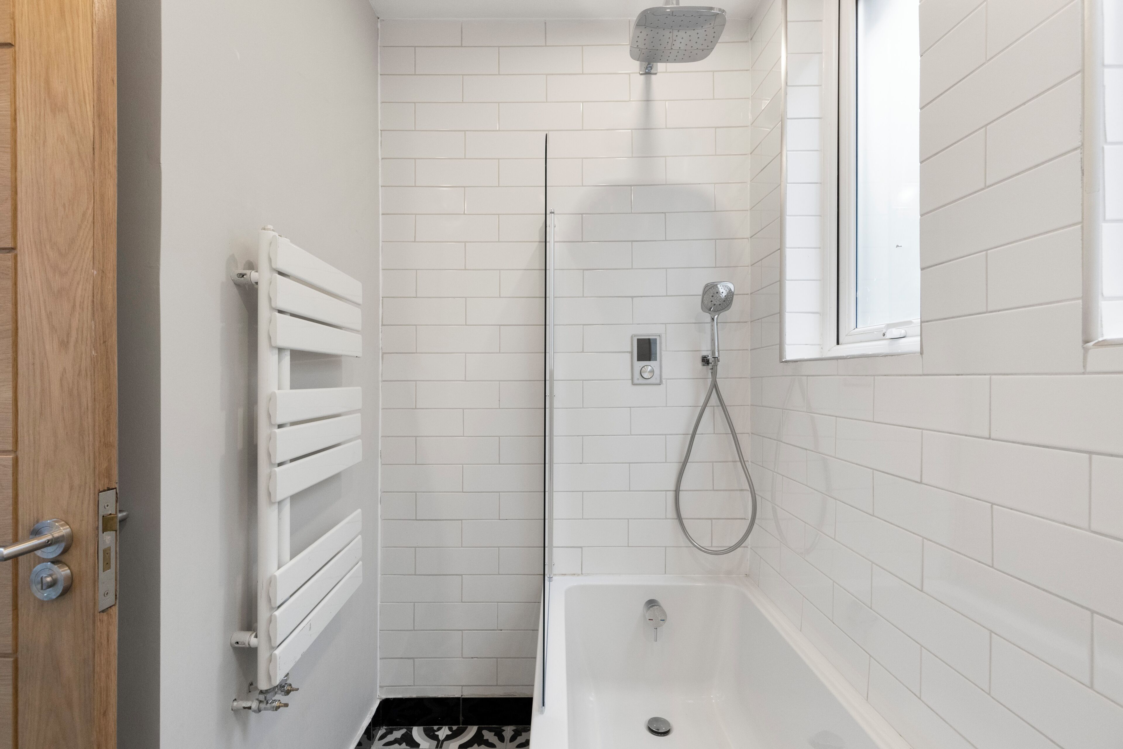 A bathroom with a shower, a bathtub, a white radiator, and a door.