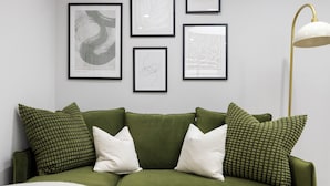 A green sofa with patterned pillows, a framed abstract painting, and a floor lamp. - Conveniently Situated - Luxuriously Furnished! (London)