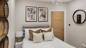 A neatly arranged bedroom with a bed, pillows, a bedside table with a lamp, a wooden door, and two framed abstract paintings on the wall. - Conveniently Situated - Luxuriously Furnished! (London)