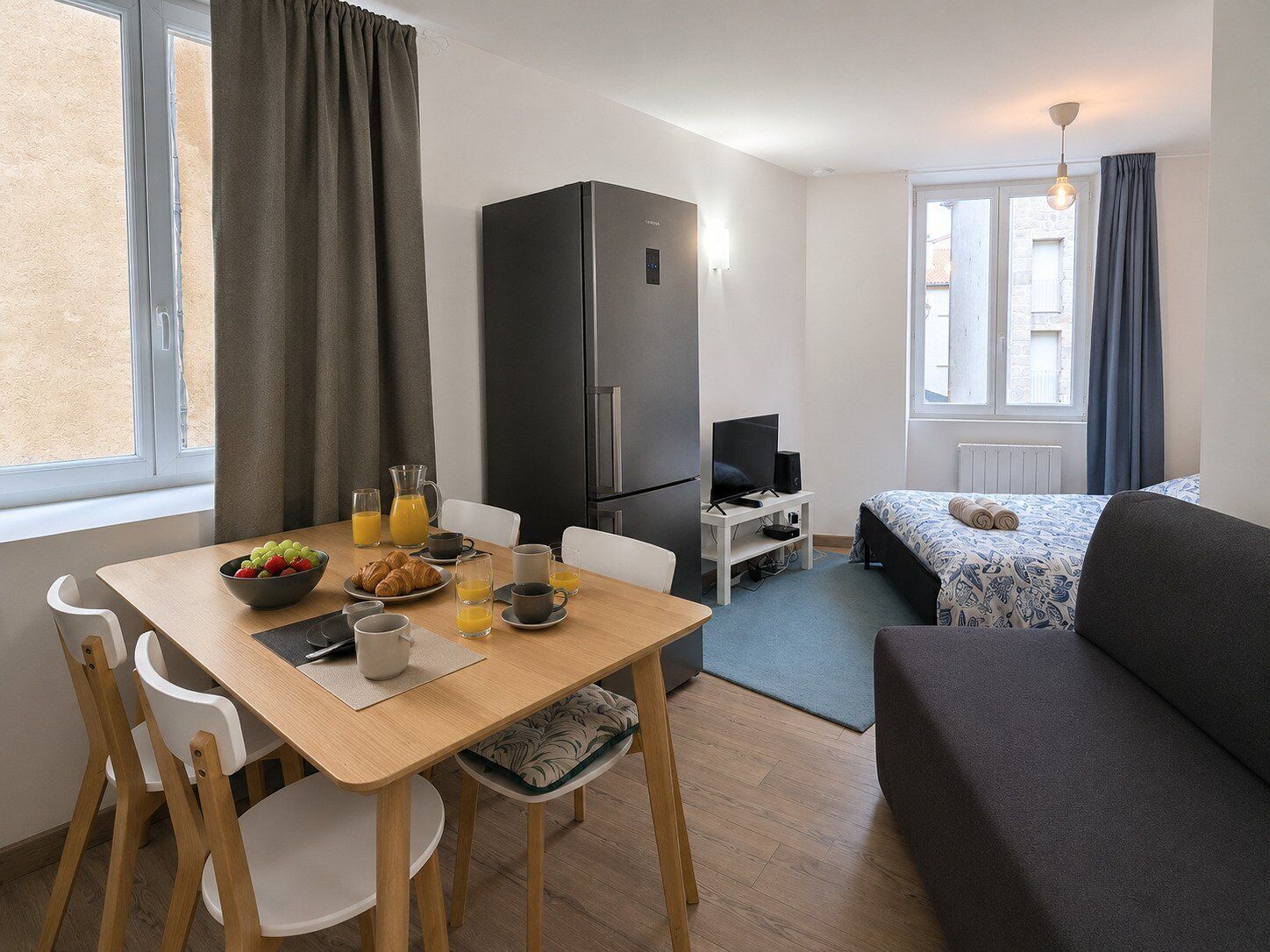 A compact room with a dining table, chairs, a sofa, a TV, and a refrigerator.
