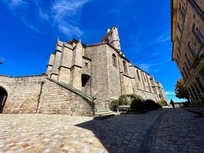 A historic stone building with a prominent tower and arched windows, situated on a cobblestone street.