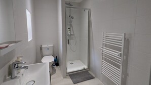 Ein modernes Badezimmer mit einer gläsernen Duschkabine, einem weißen Waschbecken und einem Handtuchhalter.
