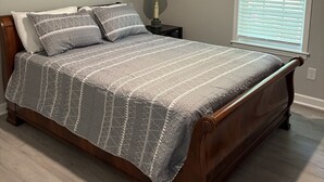 A bedroom with a bed, a nightstand, a lamp, and a window with blinds.