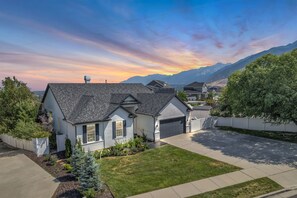 A residential house with a garage, a driveway, and a well-maintained lawn. - Draper Skyline Retreat | Hot Tub & 6BDR (Draper)