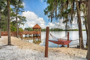 Eine Hängematte am sandigen Strand, ein Holzkiosk und ein Steg, der in den See führt.