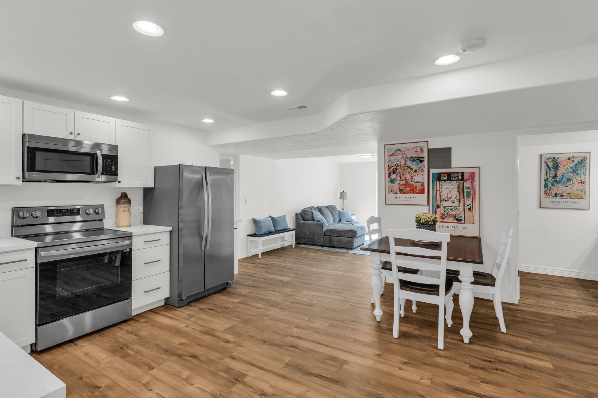 A modern kitchen with stainless steel appliances, a dining area with white furniture, and artwork on the walls.
