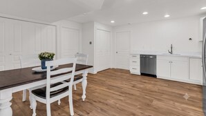 Une cuisine moderne avec des meubles blancs, un lave-vaisselle en acier inoxydable et une table à manger en bois, assortie de chaises blanches.