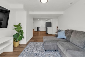 Een moderne woonkamer met een grijze bank, een grote potplant en een kamerkleed met een patroon.