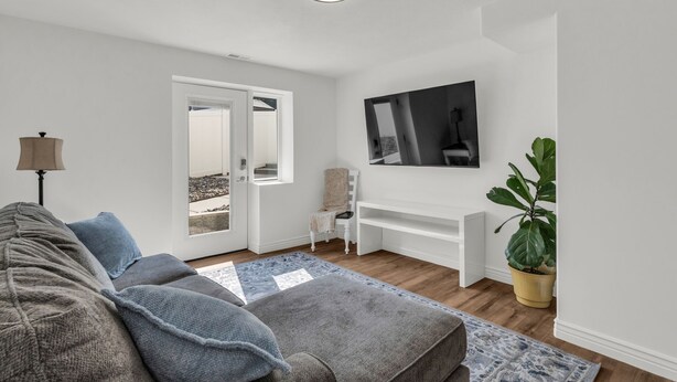 Un salon moderne avec un canapé, un téléviseur fixé au mur, une plante en pot et une porte donnant sur l’extérieur.