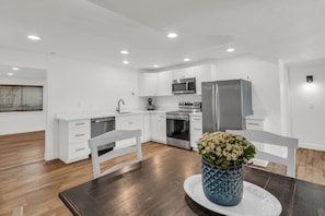 Een moderne keuken met witte kasten, roestvrijstalen apparatuur en een eettafel met stoelen.