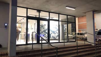 Entrada de un edificio con puertas de vidrio, una escalera y un estacionamiento con automóviles.