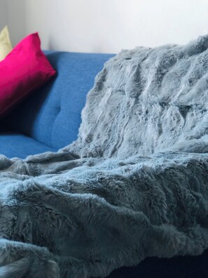 En sofa med en blå pude og et gråt, blødt tæppe.