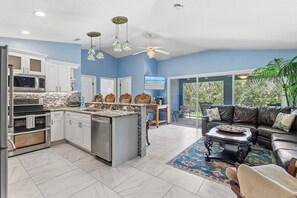 A modern kitchen with white cabinets, a central island, and a dining area with a black leather sofa and a coffee table. - The Flying Mermaid (Edgewater)