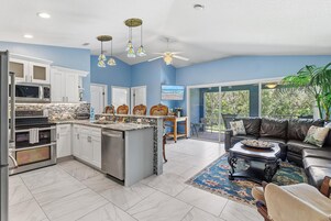 Cocina moderna con armarios blancos, una isla central y un área de comedor con sofá de cuero negro y una mesa de centro.