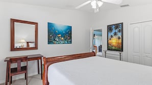 A bedroom with a bed, a desk, a chair, a ceiling fan, and two paintings on the wall. - The Flying Mermaid (Edgewater)