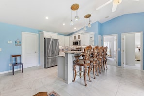 A kitchen with a central island, stainless steel appliances, and a dining area with ornate chairs. - The Flying Mermaid (Edgewater)