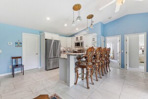 Una cocina con una isla central, electrodomésticos de acero inoxidable y una zona de comedor con sillas decorativas.