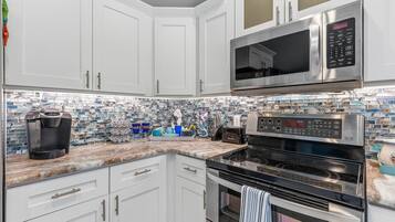A kitchen with white cabinets, a stainless steel microwave, a Keurig coffee maker, a toaster, and a tiled backsplash.