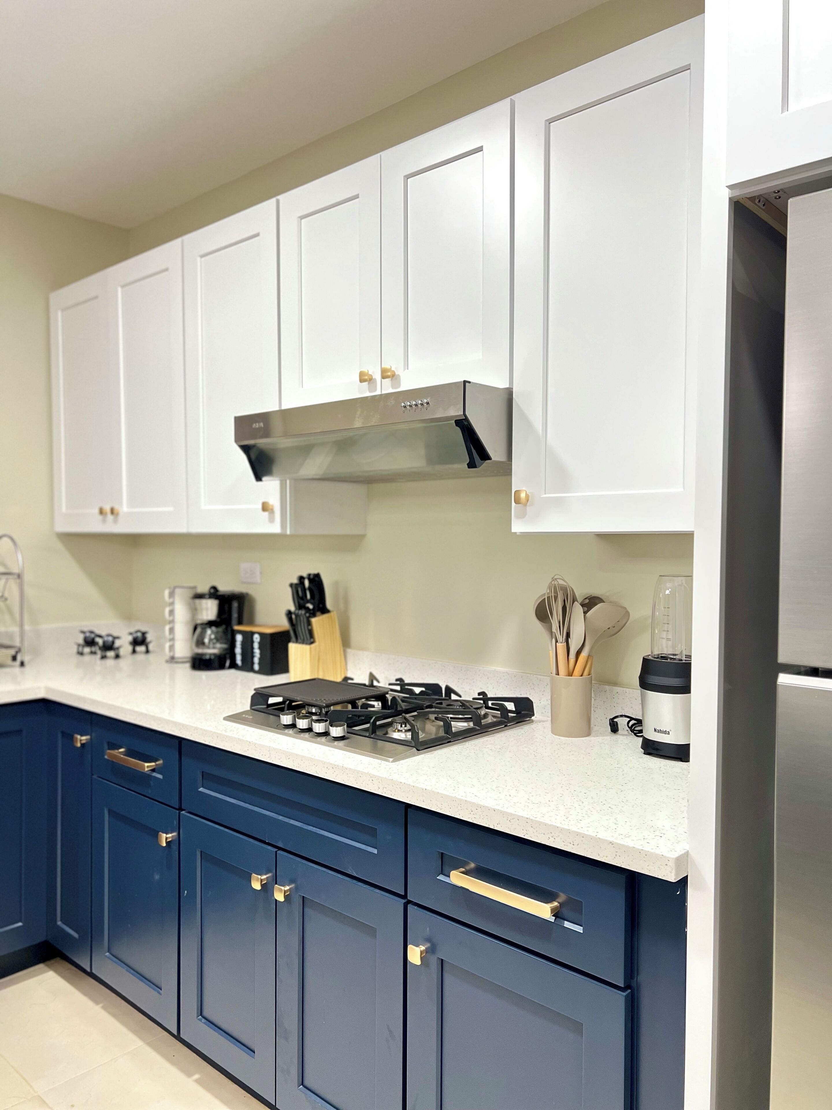 A modern kitchen with white upper cabinets, a stainless steel range hood, a gas stove, and blue lower cabinets.