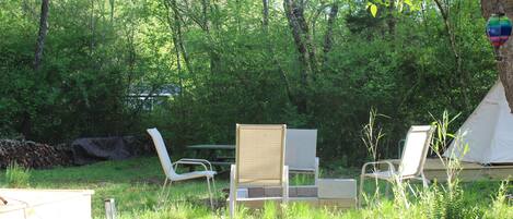 A campsite with a dog, two white chairs, a table, and a tent.