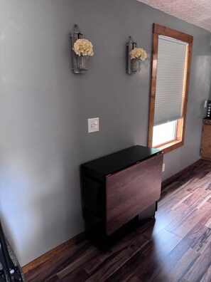 A room with a wooden cabinet, a window with blinds, and two wall-mounted flower arrangements. - Cozy 2-bedroom mobile home in tranquil Moncure with AC. (Moncure)