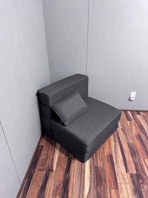 Ein Eckzimmer mit grauem Sofa, Holzboden und weißem Verteilerkasten.