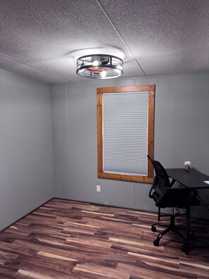 Una habitación con ventana de madera, una silla de oficina negra y una mesa.