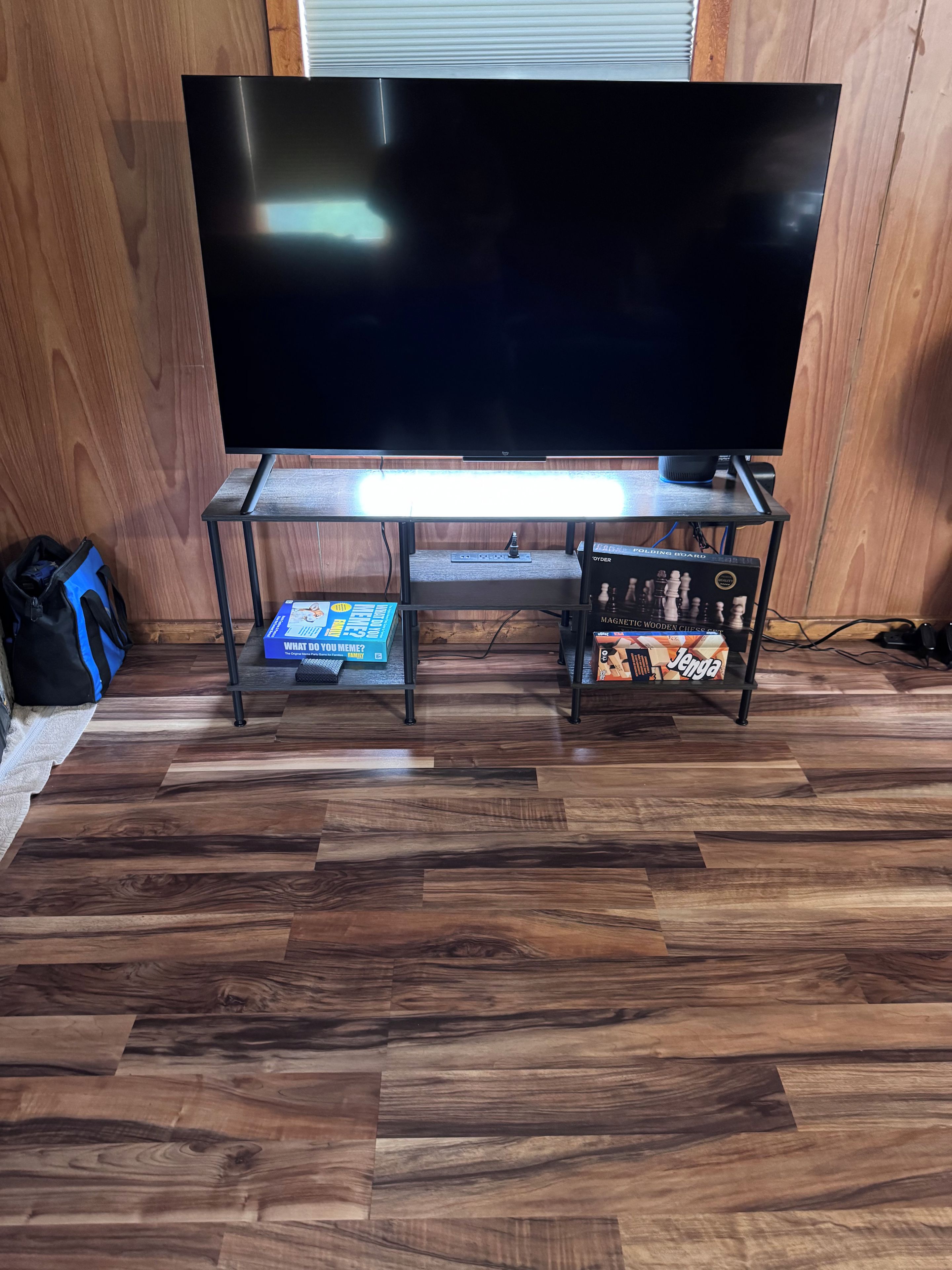 Un suelo de madera, un televisor sobre un mueble bajo, una mesita con un juego de mesa y un juego de ajedrez.
