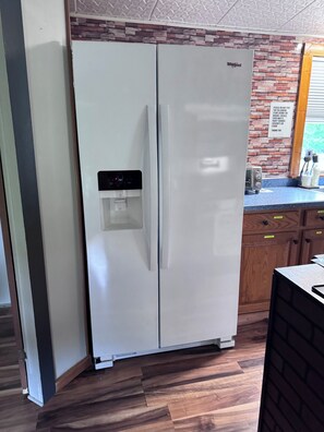 Een keuken met een witte Whirlpool koelkast, een waterdispenser en een spatwand met een bakstenen patroon.