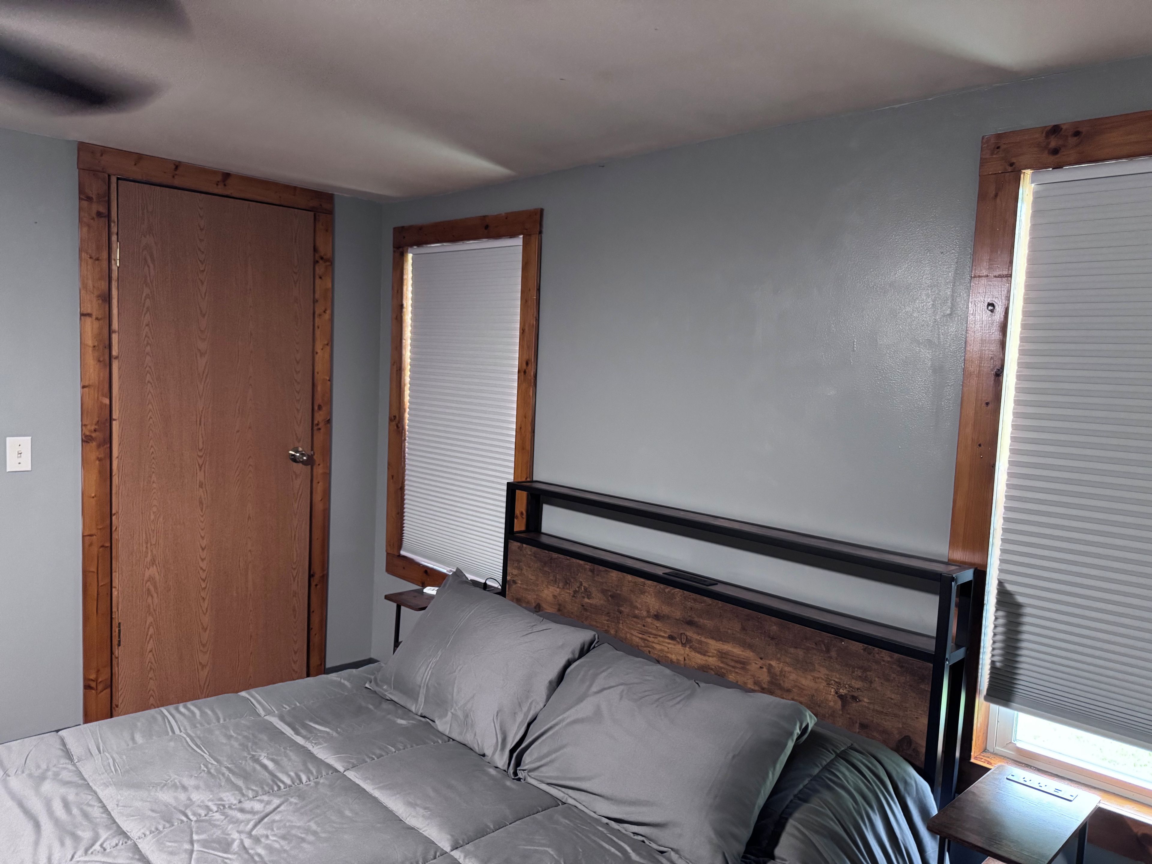 Een slaapkamer met een bed, houten hoofdbord, een raam met zonwering en een deur.