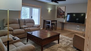 A living room with a sofa, coffee table, TV, ceiling fan, and windows with blinds. - Fantastic 5-bedroom house in lovely Bralorne BC. (Squamish-Lillooet A)