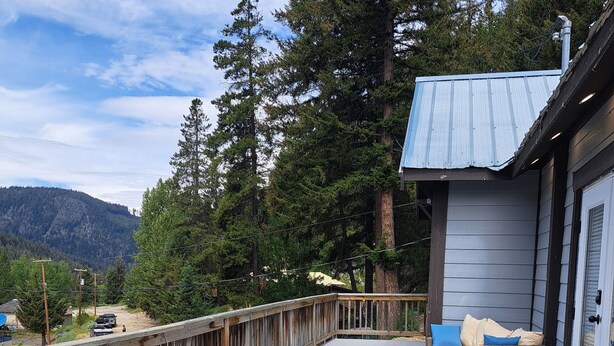 A covered outdoor patio with wicker furniture, a table, and a view of a mountain. - Fantastic 5-bedroom house in lovely Bralorne BC. (Squamish-Lillooet A)