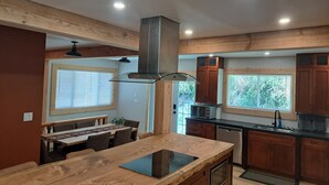 A modern kitchen with wooden cabinetry, a central island with a built-in stovetop, and a dining area with a table and chairs. - Fantastic 5-bedroom house in lovely Bralorne BC. (Squamish-Lillooet A)