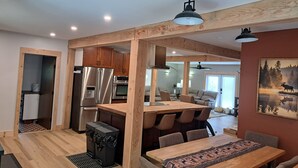 A modern kitchen with stainless steel appliances, a dining area with a wooden table and chairs, and a large painting on the wall. - Fantastic 5-bedroom house in lovely Bralorne BC. (Squamish-Lillooet A)